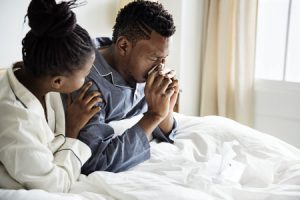 A man in bed with his significant other sneezing because of black mold