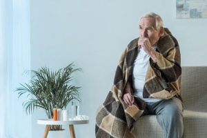 older man with blanket coughing inside