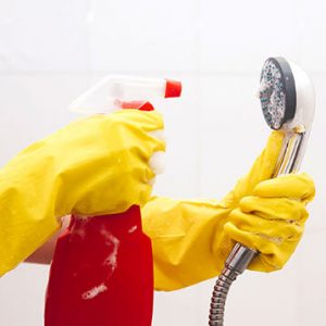 person in yellow gloves cleaning the shower head to remove mold